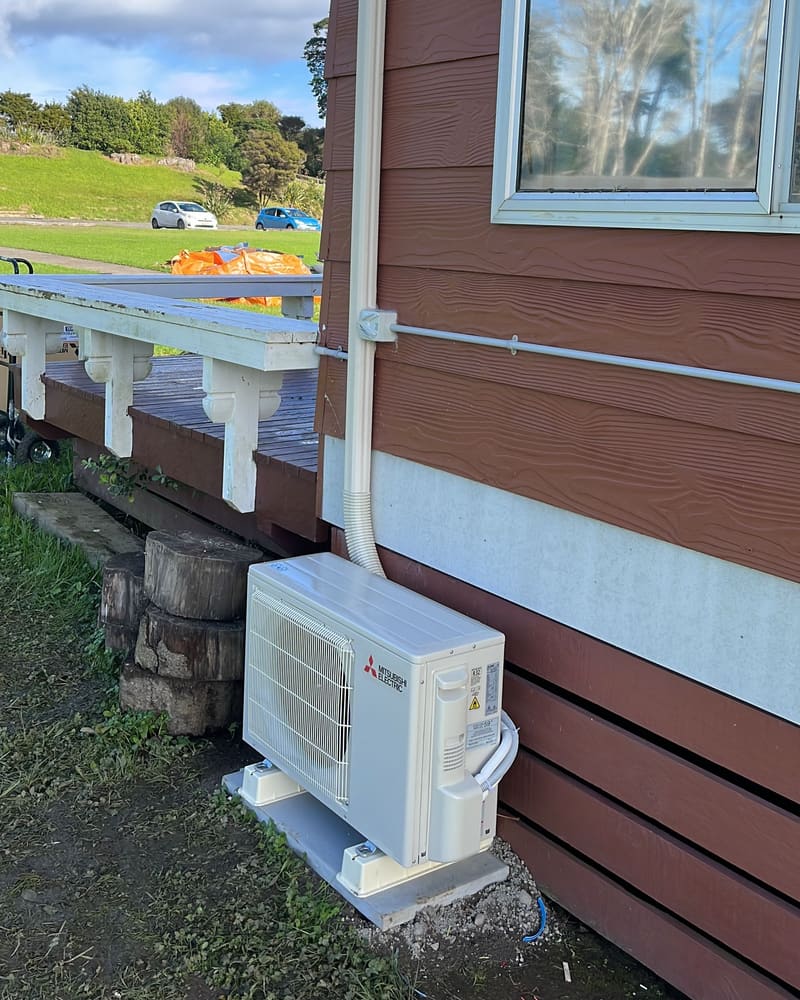 Outdoor unit sitting level beside a deck, with the pipe cover running up the wall