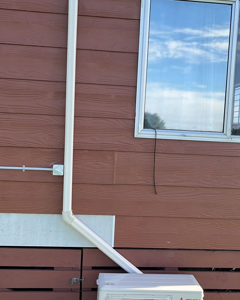Heat pump pipework run neatly in a cover along weatherboard cladding